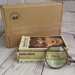 A stack of vintage Agatha Christie novels with a magnifying glass, next to a brown card postal box